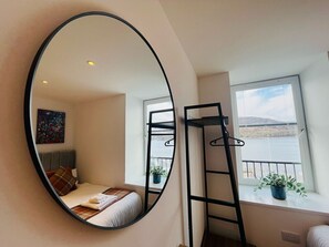 A bedroom with a bed, a mirror, a window with a view of the sea, and a ladder.