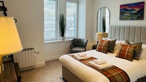 A modern bedroom with a large bed, a chair, a radiator, and a window with blinds. - Bramble Apartment in Fort William Town Centre (Fort William)