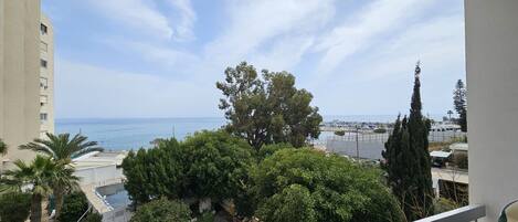 A balcony with a view of the sea, a tree, and a building.