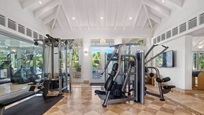 A gym with various exercise machines, a bench, and a large window offering a view of the outdoors. - Bahia Beach Steps from Ocean 3BDRM- Ocean View (Herreras)