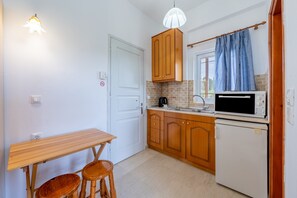 Une cuisine compacte avec des meubles en bois, un réfrigérateur blanc, un four à micro-ondes, un évier et une table en bois accompagnée de deux tabourets.
