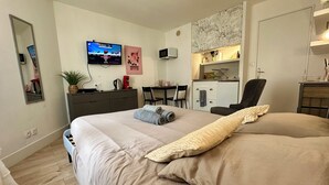 A hotel room with a large bed, a desk with a computer, a TV on the wall, and a kitchenette. - Studio in the heart of Dijon (Dijon)