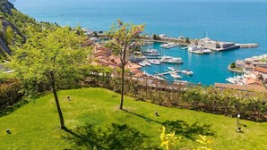 A coastal marina with boats, a lighthouse, and a hilly backdrop.