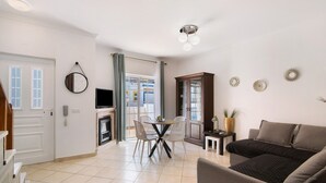 Un salon comprenant un canapé, une table à manger avec des chaises, un téléviseur, une cheminée et une porte donnant sur une autre pièce.
