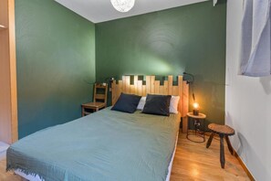 A bedroom with a bed, a nightstand, a chair, and a small table with a lamp.