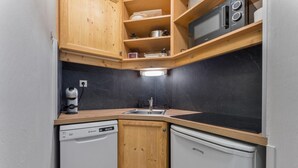 Cocina compacta con armarios de madera, un microondas, un lavabo y un lavavajillas.