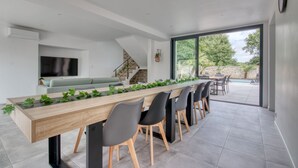 A modern kitchen with a long wooden table, black chairs, and a view of the outdoor patio. - Le Logis de la Pierre Bleue - Maison climatisée avec piscine (Férel)