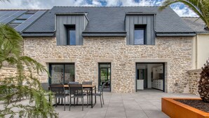 A stone house with a patio, a dining area, and a garage. - Le Logis de la Pierre Bleue - Maison climatisée avec piscine (Férel)