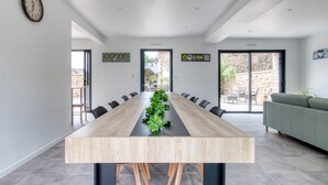 A modern dining area with a long wooden table, black chairs, and a green plant centerpiece. - Le Logis de la Pierre Bleue - Maison climatisée avec piscine (Férel)