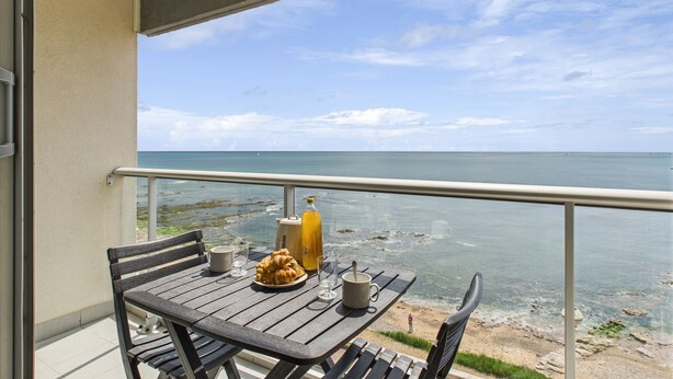 A balcony with a table set for two, overlooking a beach with clear skies.