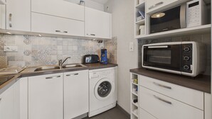 A compact kitchen with white cabinets, a washing machine, a microwave, and a toaster.