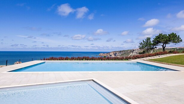 A rectangular swimming pool with a clear view of the ocean and rocky cliffs in the background.