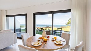A dining area with a table set for breakfast, large windows with a view of the sea, and a balcony with outdoor seating.