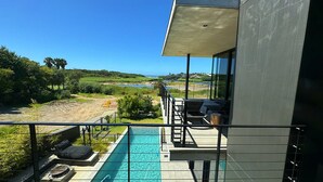 Un edificio moderno con un balcone che si affaccia su una piscina e una vista panoramica dell'oceano e delle colline.