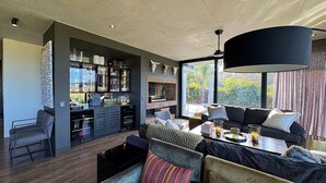 Un soggiorno moderno con angolo bar, posti a sedere confortevoli e una grande finestra con vista sul verde.
