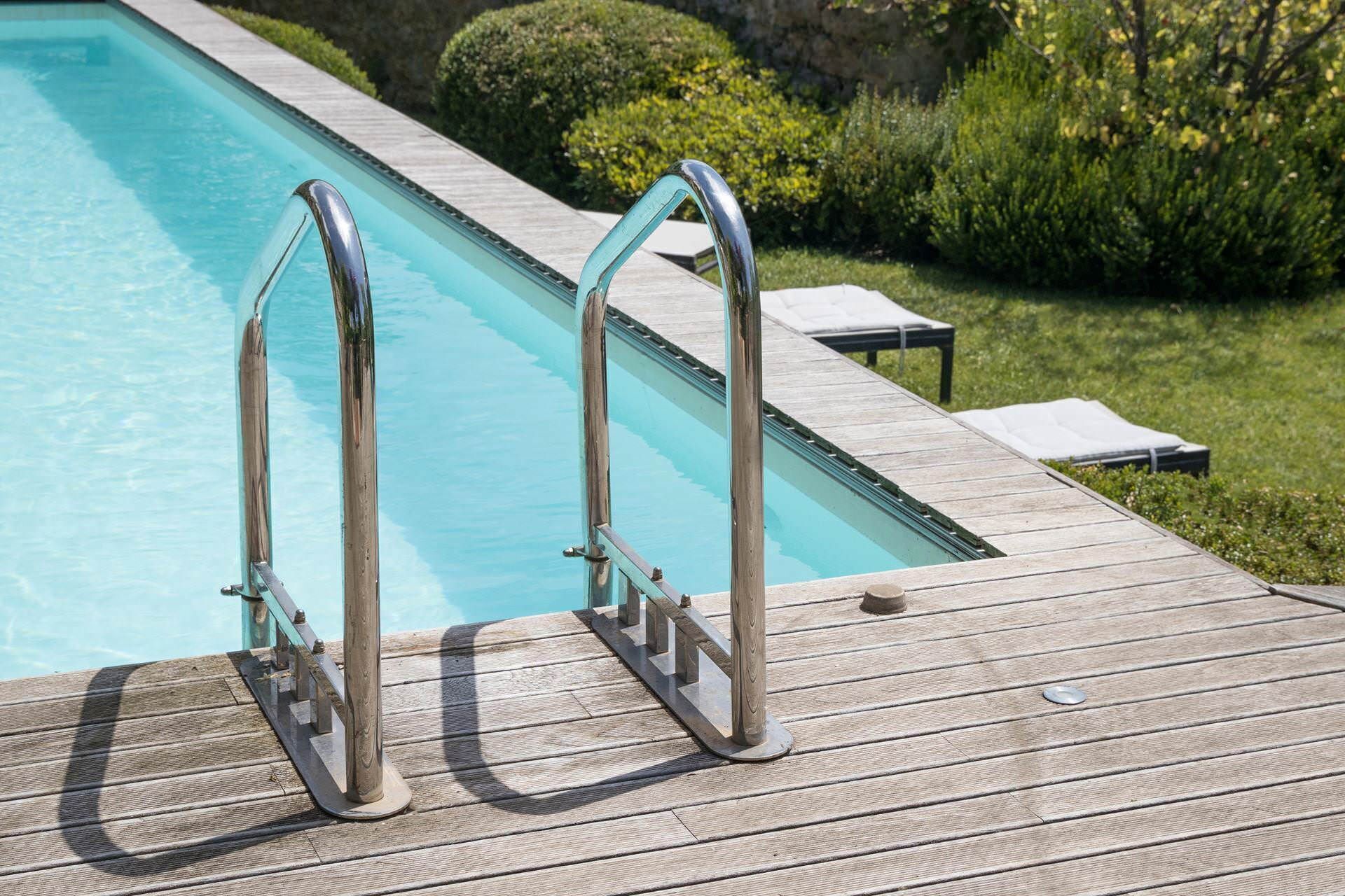A wooden deck with a poolside area, including metal pool ladders and a small table with a chair.
