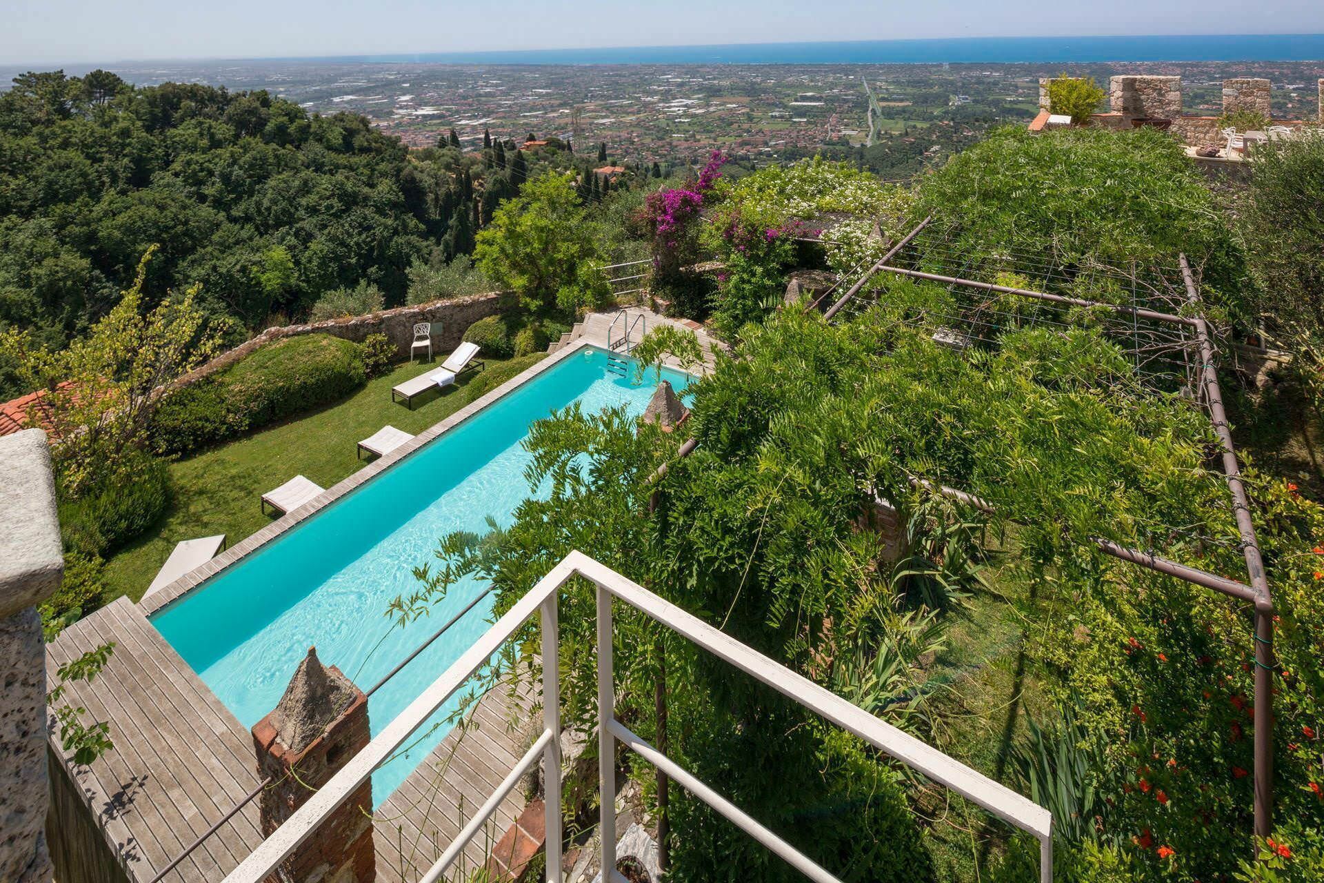 Una piscina con vistas a un paisaje urbano, rodeada de exuberante vegetación y estructuras de piedra.