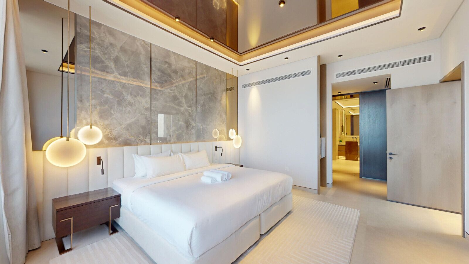 A modern hotel room with a large bed, a nightstand, and a mirror. There is a door leading to another room.