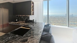A modern kitchen with a marble countertop and a large window offering a city view.
