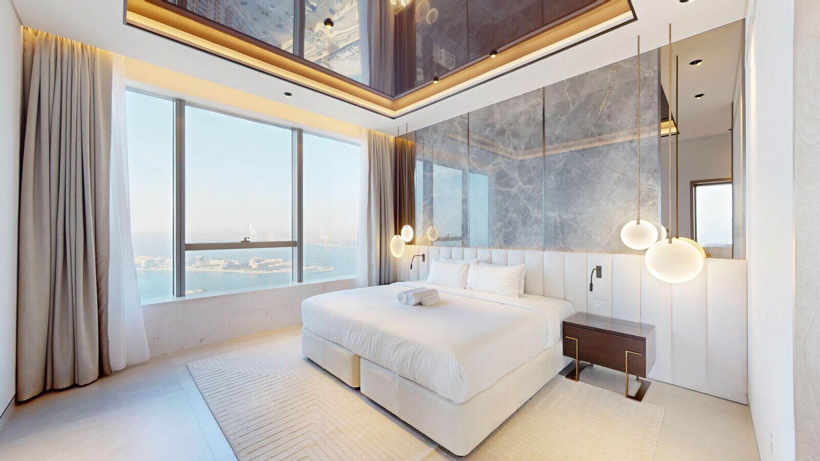 A modern bedroom with a large bed, a nightstand, a mirror, and a view of the city.