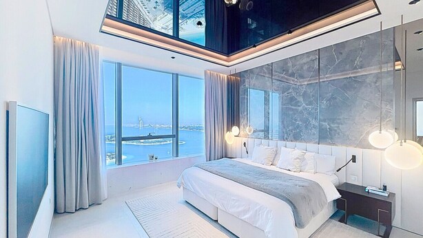 A modern bedroom with a large bed, a TV, and a view of a cityscape.
