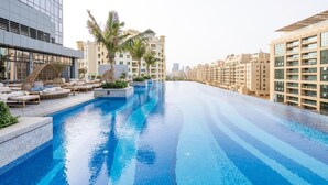 A swimming pool with lounge chairs and palm trees, surrounded by modern buildings.