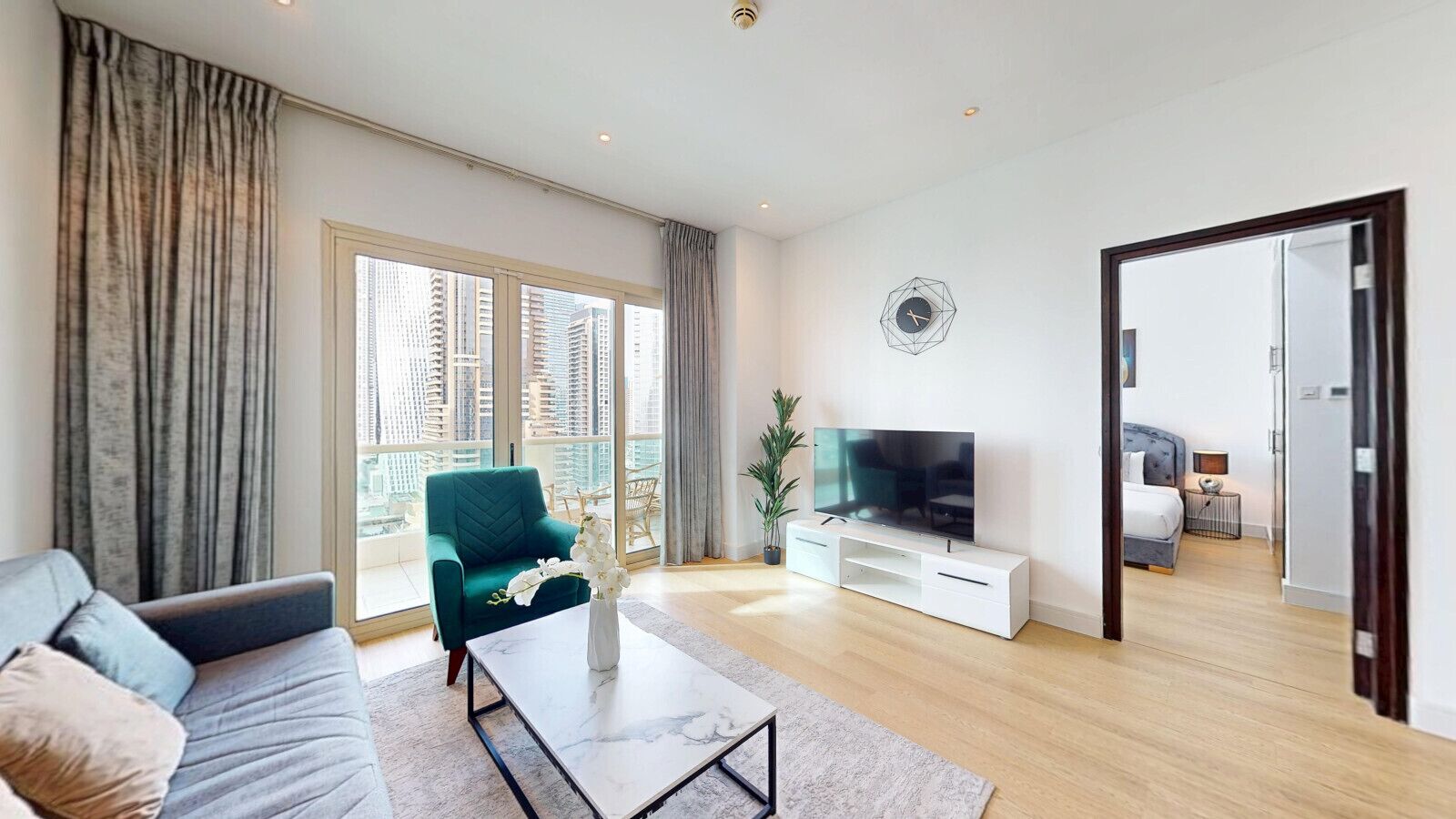 Un salon moderne avec un canapé, un fauteuil turquoise, une table basse et un téléviseur posé sur un meuble blanc.