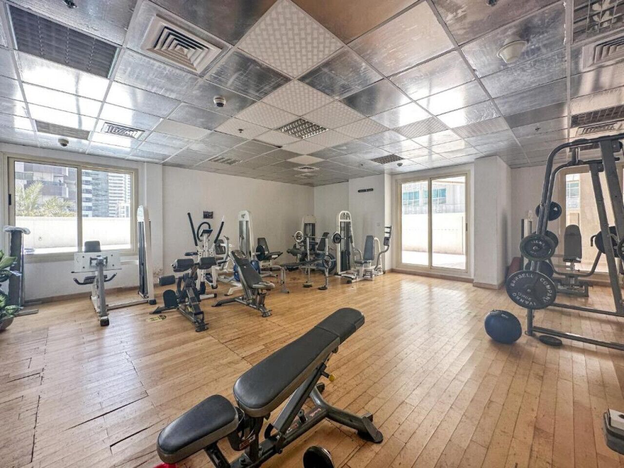Une salle de sport équipée de divers appareils d’exercice, dotée de planchers en bois et de grandes fenêtres.