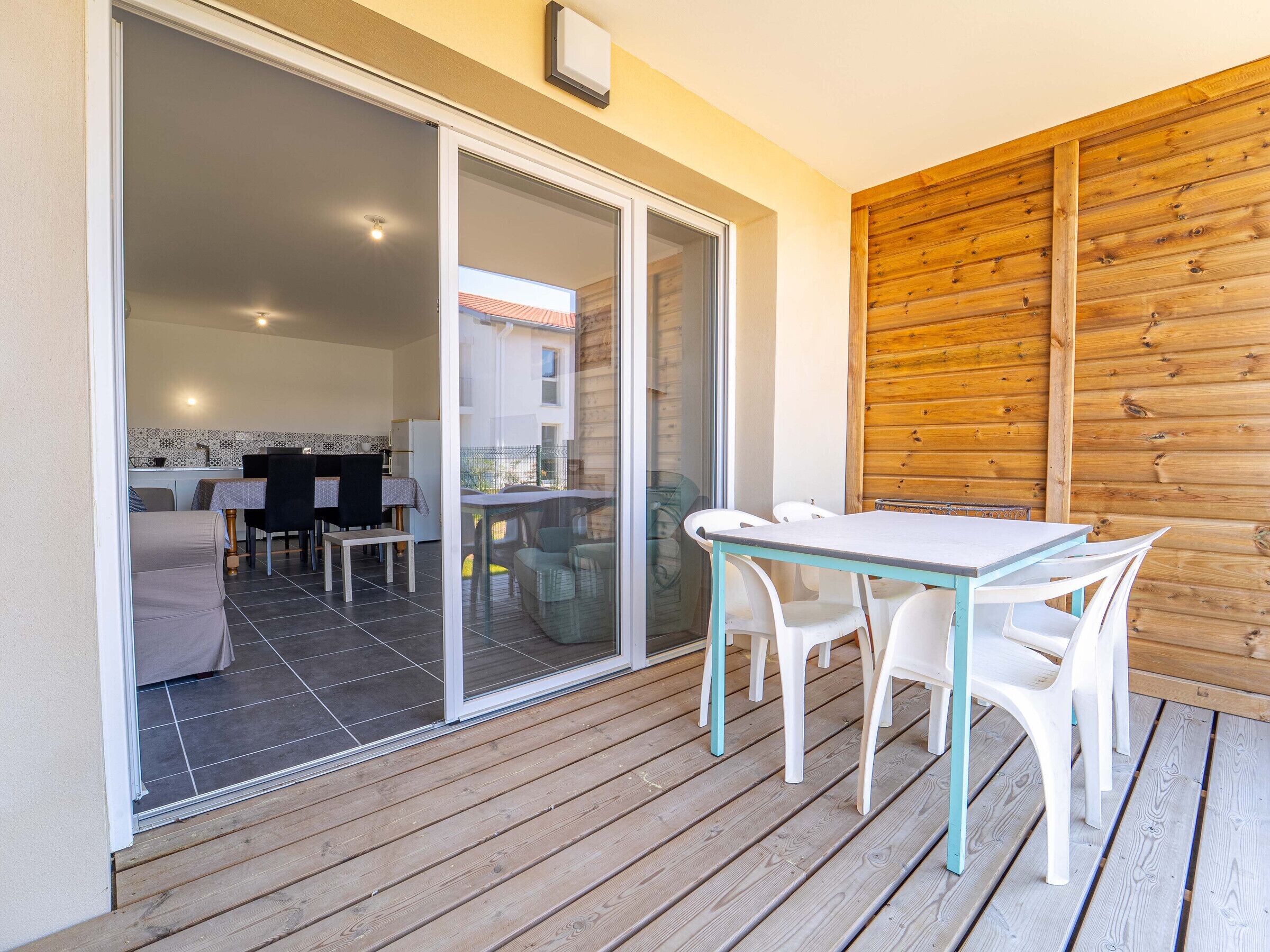 Eine Terrasse mit Tisch und Stühlen, eine Schiebetür, die auf einen Balkon führt, und eine Holzwand.