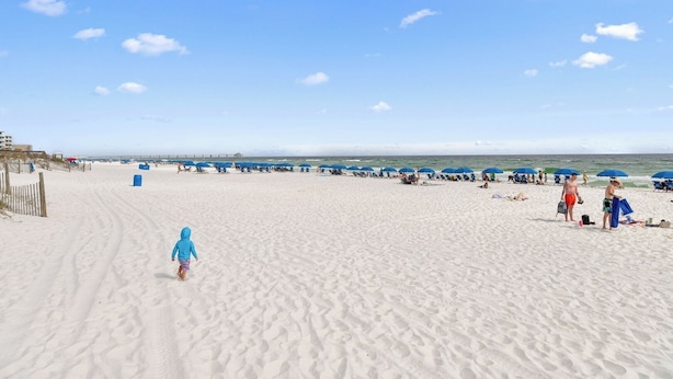 Une vaste plage de sable fin, bordée de rangées de parasols bleus et de chaises de plage, un ciel dégagé et des empreintes de pas dans le sable.