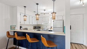 Une cuisine moderne avec des meubles blancs, un îlot central doté de tabourets et des luminaires suspendus.