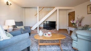 A living room with a TV, two sofas, a coffee table, and a staircase.