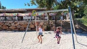A sandy beach area with a swing set and a stone wall in the background.