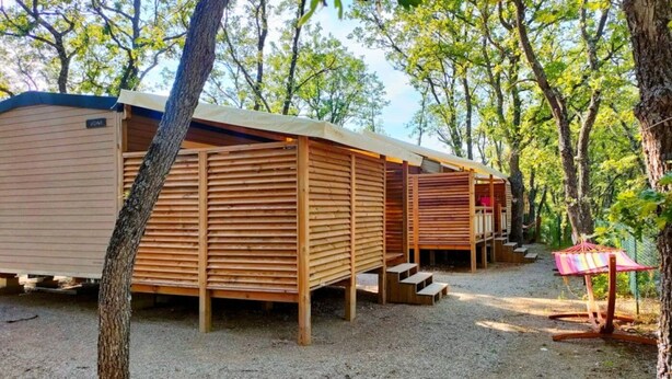 A row of wooden mobile homes with a gravel ground, surrounded by trees.