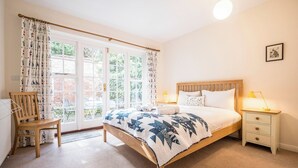 A bedroom with a wooden bed, a nightstand with a lamp, a chair, and a window with curtains.