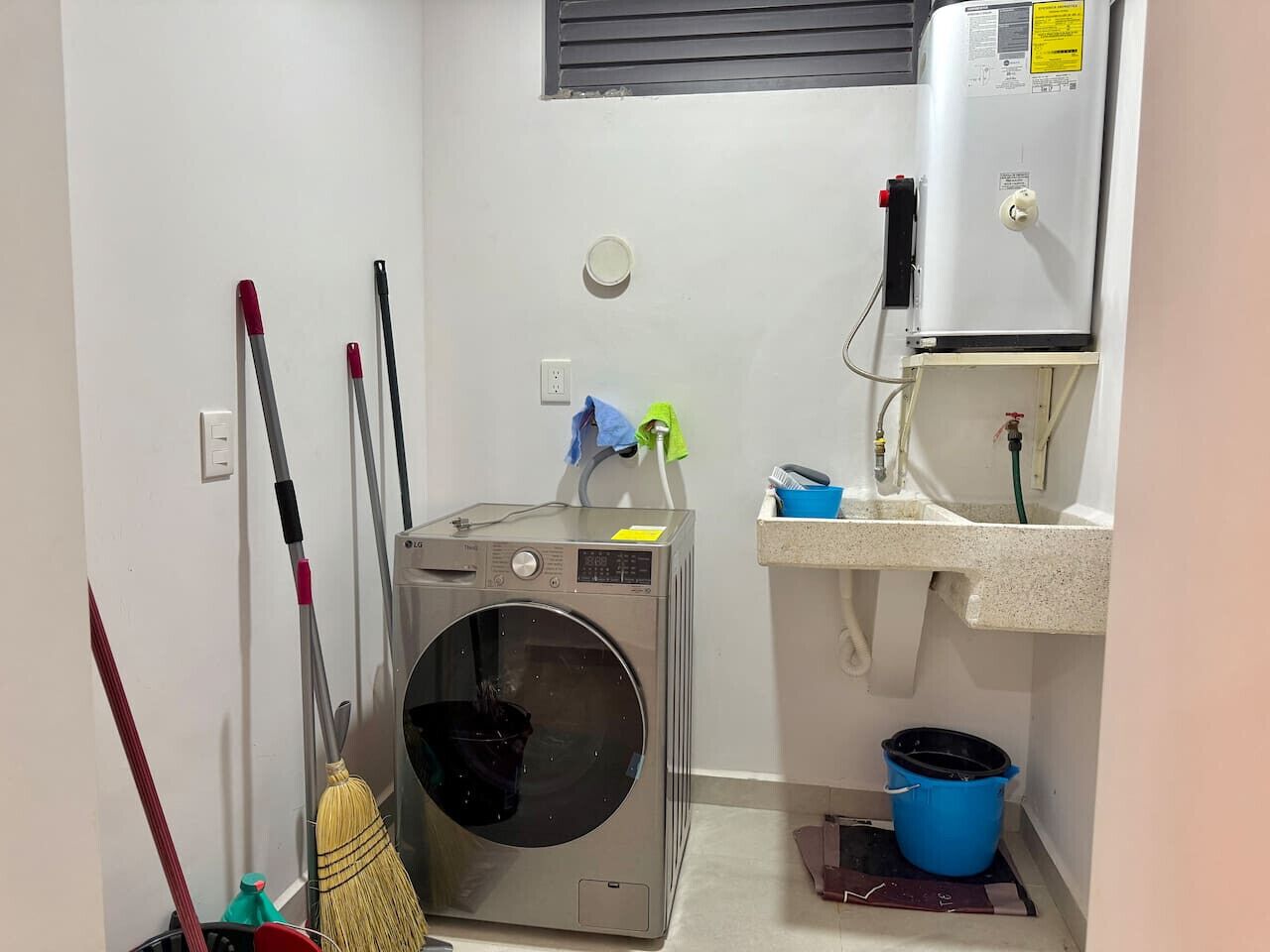 A compact laundry room with a front-loading washing machine, a sink, and a mop.