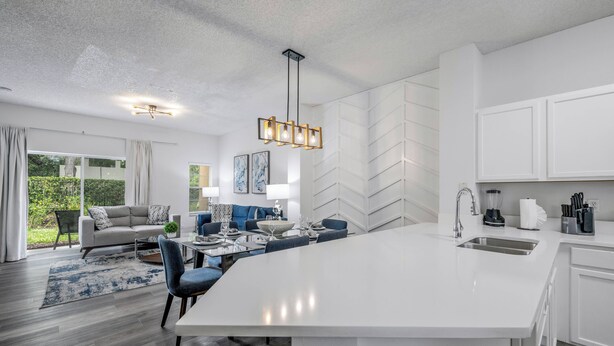 A modern kitchen with white cabinetry, a large island, and a dining area with blue chairs.