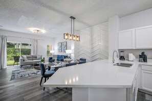 A modern kitchen with white cabinetry, a large island, and a dining area with blue chairs.