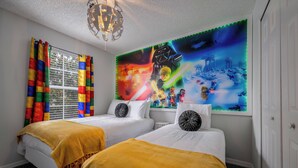 A hotel room with two beds, colorful curtains, a large wall mural, and a chandelier.