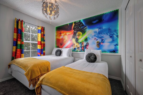 A hotel room with two beds, colorful curtains, a large wall mural, and a chandelier.