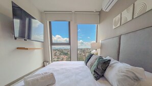 Une chambre d’hôtel avec un grand lit, un téléviseur à écran plat fixé au mur et une vue sur la ville par la fenêtre.