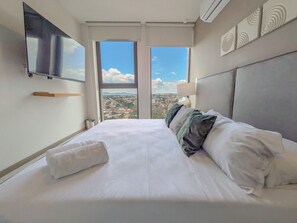 Ein Hotelzimmer mit einem großen Bett, einem wandmontierten Flachbildfernseher und Blick auf die Stadt durch das Fenster.