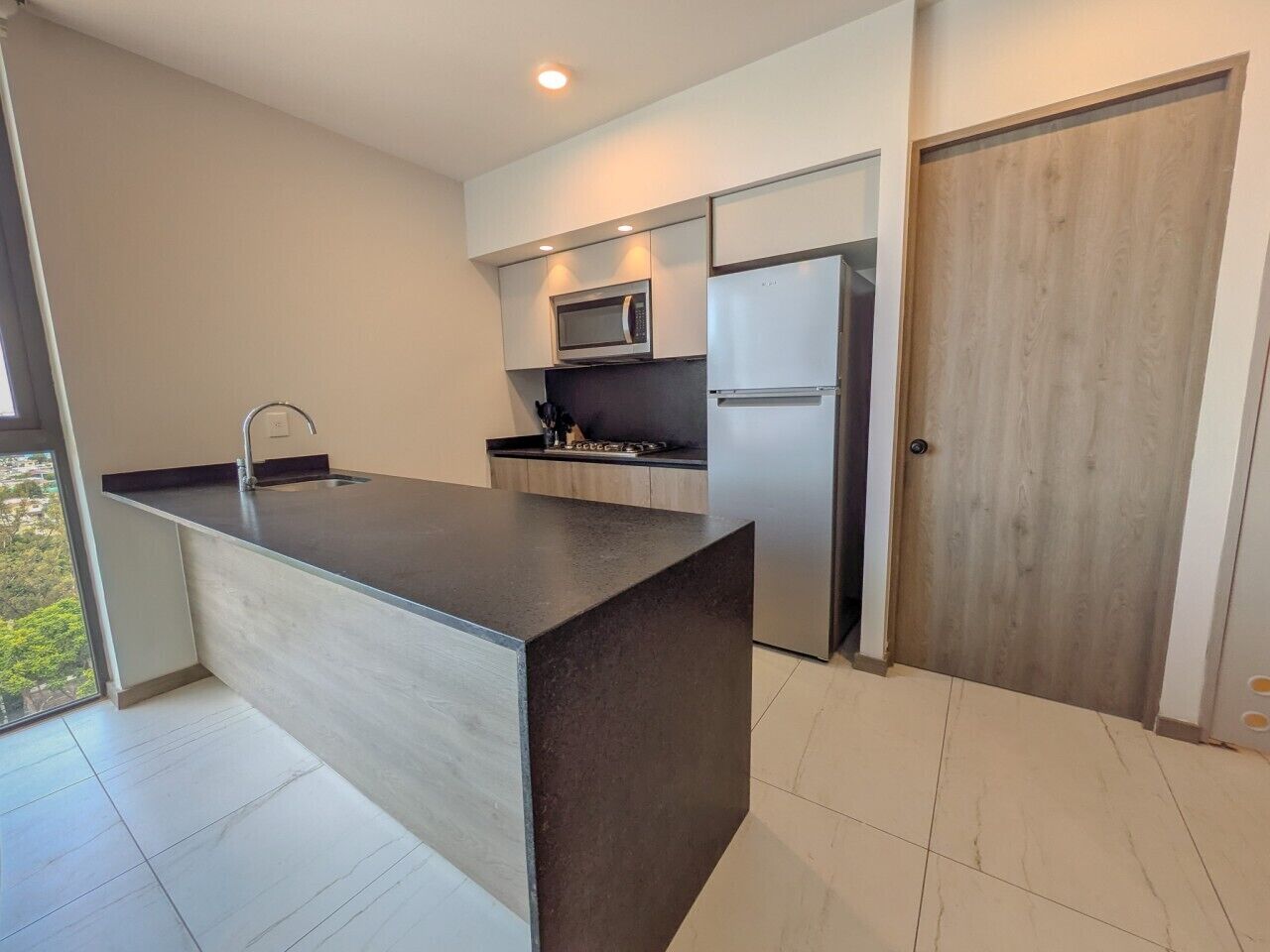 A modern kitchen with a central island, stainless steel appliances, and a sliding wooden door.