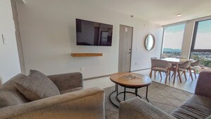 Un salon moderne doté d’un téléviseur à écran plat fixé au mur, d’une table basse ronde et d’un coin repas avec des chaises.