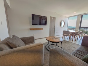 Ein modernes Wohnzimmer mit einem flachbildfernseher an der Wand, einem runden Couchtisch und einem Essbereich mit Stühlen.