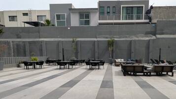 An outdoor seating area with tables and chairs, a fire pit, and a view of buildings in the background.