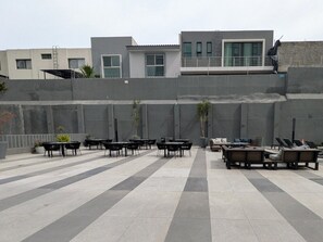 An outdoor seating area with tables and chairs, a fire pit, and a view of buildings in the background.