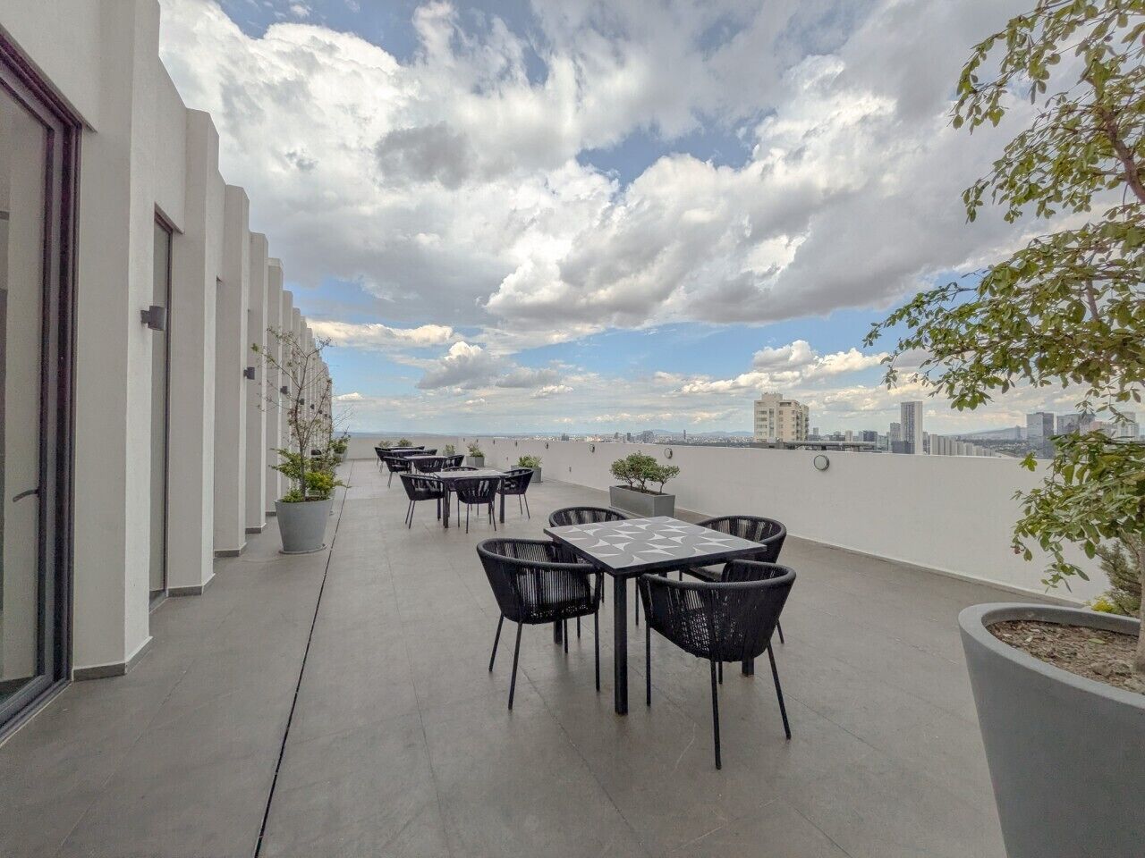 Una terraza en la azotea con mobiliario exterior, vistas del horizonte urbano y una hilera de edificios a un lado.