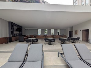 Eine Dachterrasse mit Liegestühlen und Tischen, einem Küchenbereich und Blick auf die Stadt.