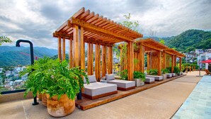 A rooftop terrace with wooden pergolas, cushioned seating, and potted plants.